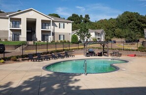 A pool area with lounge chairs and a covered seating area, surrounded by a fence.