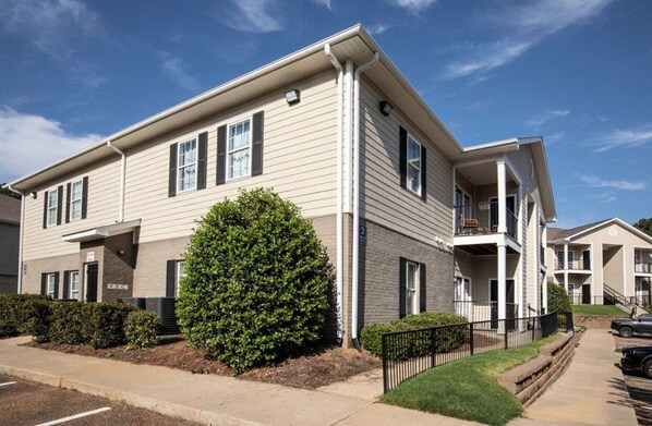 A two-story apartment building with a flat roof, a covered front porch, and a small front yard with a hedge.