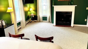 A hotel room with a fireplace, a television, a small table with a lamp, and a window with curtains.