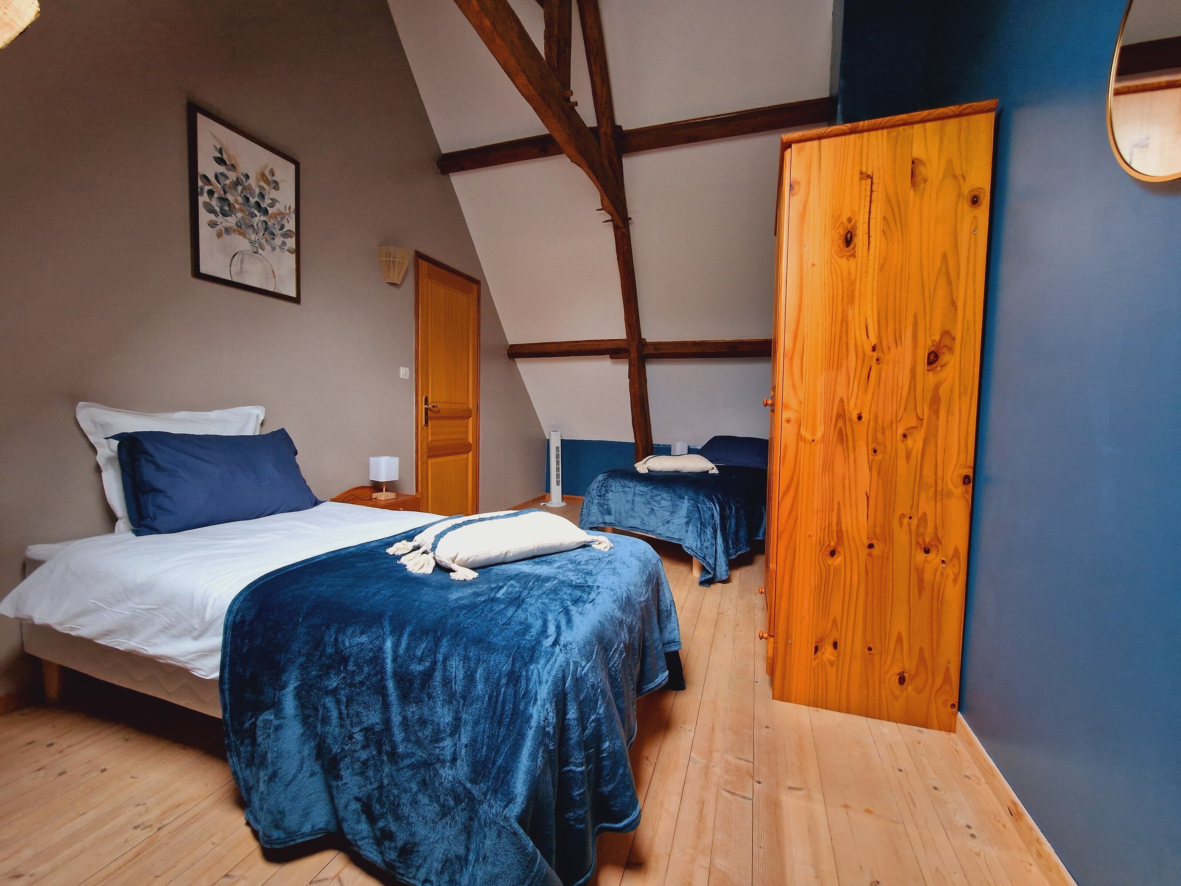 Un dormitorio con dos camas, vigas de madera, un armario de madera y un cuadro en la pared.