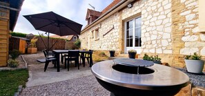 An outdoor patio area with a stone building, a table with chairs, a large umbrella, and a grill.