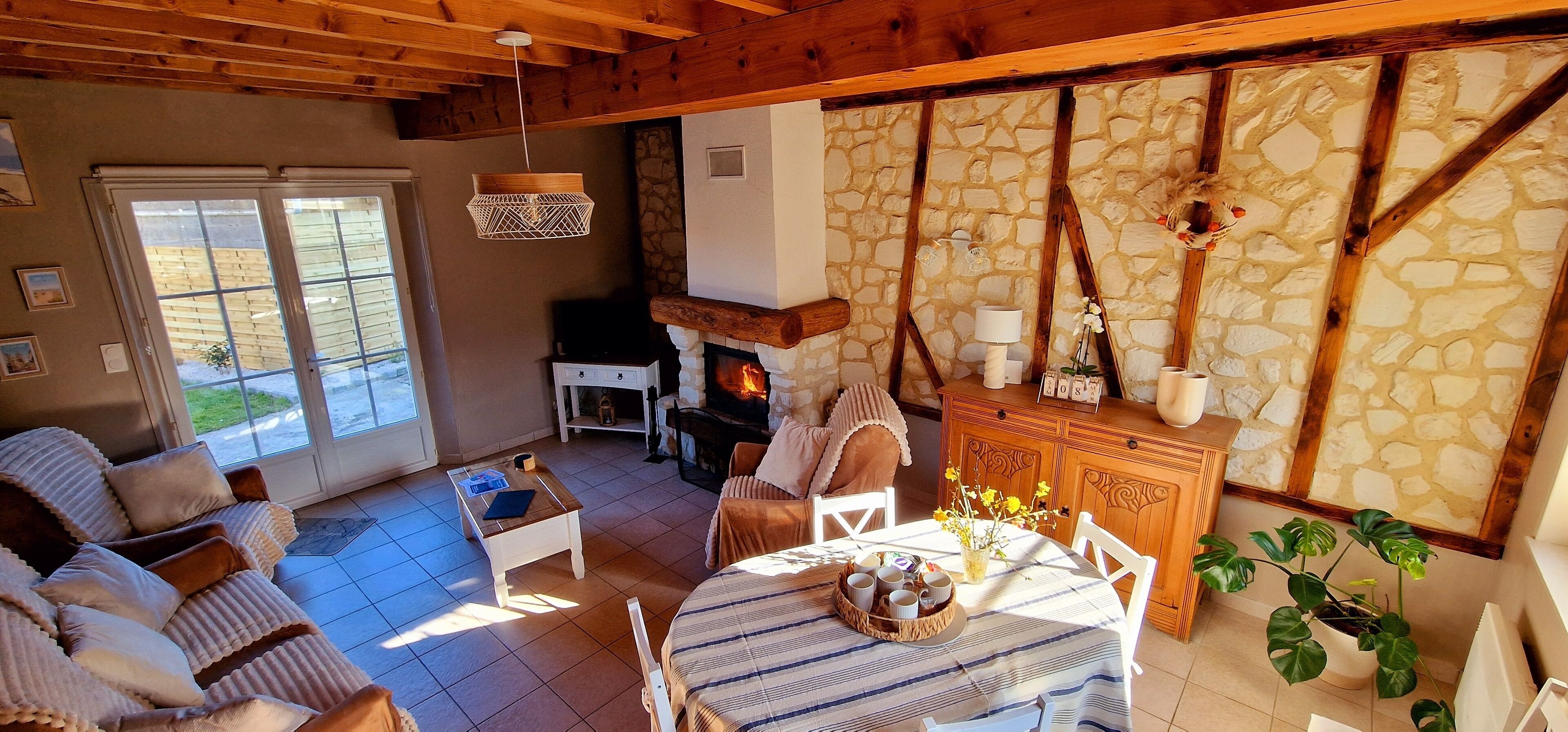 Ein gemütliches Wohnzimmer mit Kamin, Holzbalken, Steinwänden und einem Essbereich mit gedecktem Tisch.