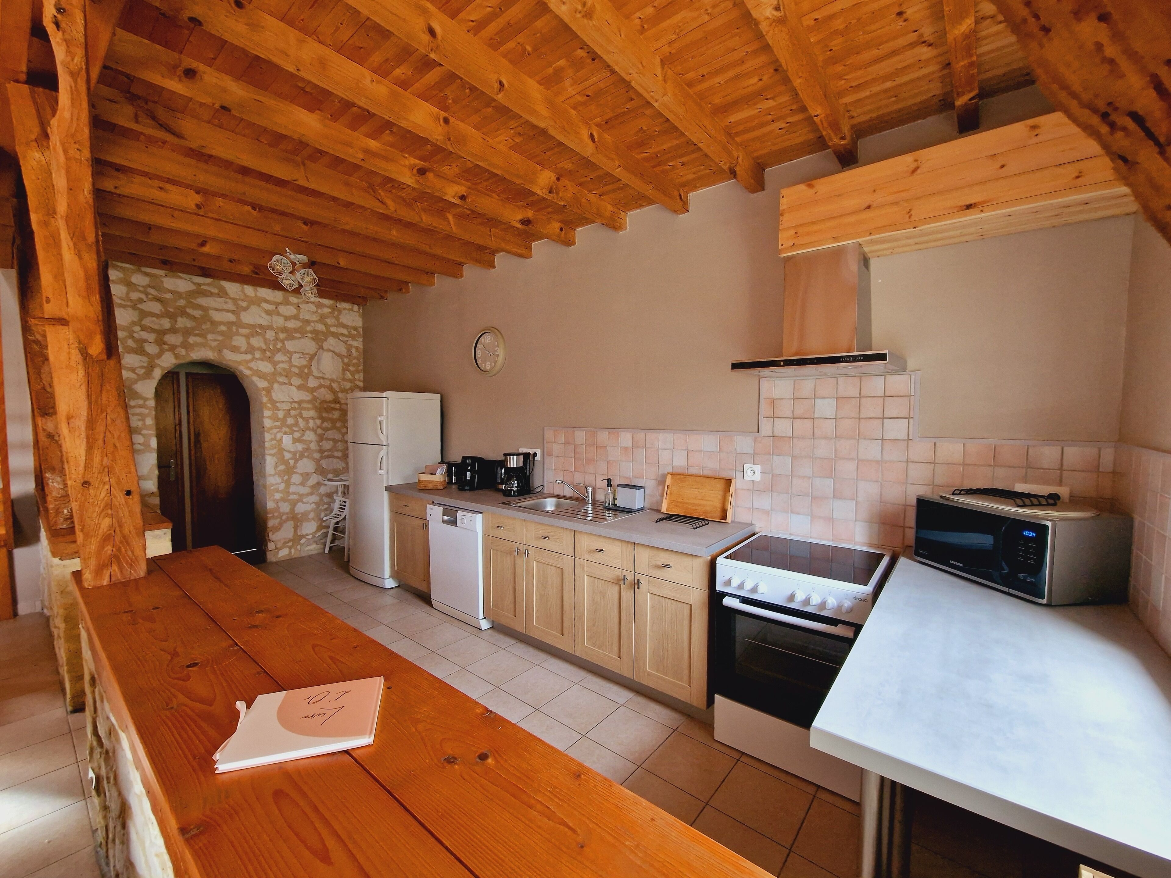 A compact kitchen with wooden beams, a stone archway, a white refrigerator, a stove, and a microwave.
