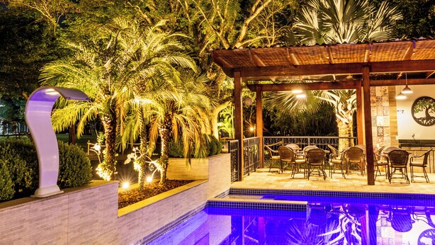 Un espace extérieur avec piscine, accessible la nuit, doté d’un sol carrelé, d’une pergola et de sièges placés sous une tonnelle.