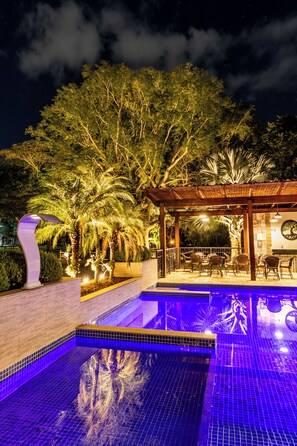A nighttime outdoor pool area with tiled flooring, a pergola, and seating under a canopy. - Pousada Rainha da Mata (Itatiaia)