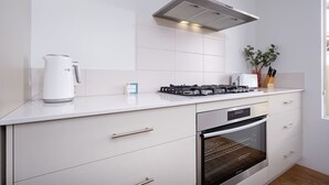 Une cuisine moderne équipée d’une cuisinière à gaz, d’un four, de meubles blancs et d’une hotte en acier inoxydable.
