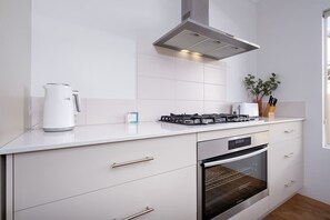 Een moderne keuken met een gasfornuis, oven, witte kastjes en een roestvrijstalen afzuigkap.