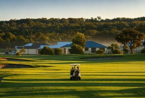 Een golfbaan met clubhuis, bomen en heldere lucht.