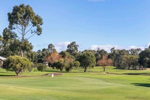 Un campo de golf con cielo despejado, árboles y un edificio al fondo.