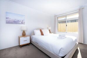 Une chambre à coucher avec un lit, des tables de chevet, une fenêtre avec des rideaux et un tableau au mur.