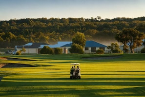 Een golfbaan met clubhuis, bomen en heldere lucht.