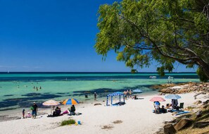Une plage avec une eau turquoise et limpide, des gens qui se baignent et des parasols sur le sable.