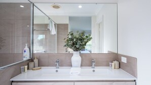 Een moderne badkamer met een grote spiegel, twee wastafels, een witte vaas met een plant en een handdoek op het aanrecht.