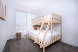 Een stapelbed met een ladder, een nachtkastje en een raam met gordijnen.