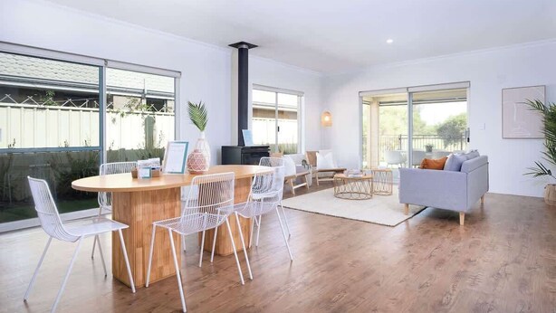 Un salon moderne avec une table à manger en bois, des chaises blanches, un canapé gris et de grandes fenêtres.
