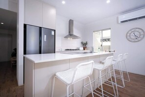 Una cocina moderna con una isla central, taburetes de bar blancos, electrodomésticos de acero inoxidable y un reloj fijado a la pared.