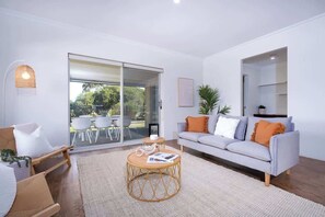 Een moderne woonkamer met een bank, een rond bijzettafeltje en een stoel. Er is een schuifdeur die leidt naar een buitenruimte met stoelen.