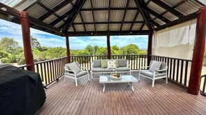 A covered outdoor deck with a sofa and chairs, a table, and a grill.