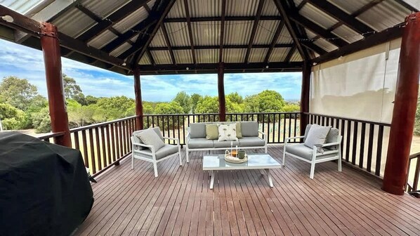 A covered outdoor deck with a sofa and chairs, a table, and a grill.