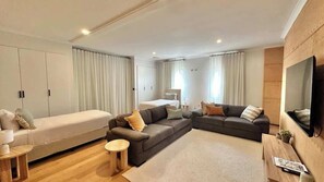 A modern hotel room with a large bed, a sofa, a TV, and a wooden floor.