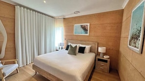 A bedroom with a wooden headboard, a bed with pillows, a nightstand with a lamp, and a chair. - Meelup Mia: The Dream Down South Beach Getaway (Dunsborough)