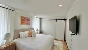 Una habitación de hotel moderna con cama, televisor de pantalla plana, mesita de noche y ventana con cortinas.