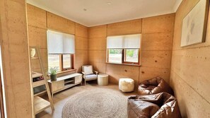 Una habitación con pared de madera, alfombra redonda, una silla blanca, un sofá de cuero marrón y una pequeña mesa con una planta.