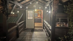 Houten lodge-ingang met een bord, een deur met raam, en een houten trap die naar binnen leidt.
