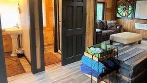 Een gezellig interieur van een blokhut met een houten vloer, een zwarte deur, een bankje en een wiel op de achtergrond.