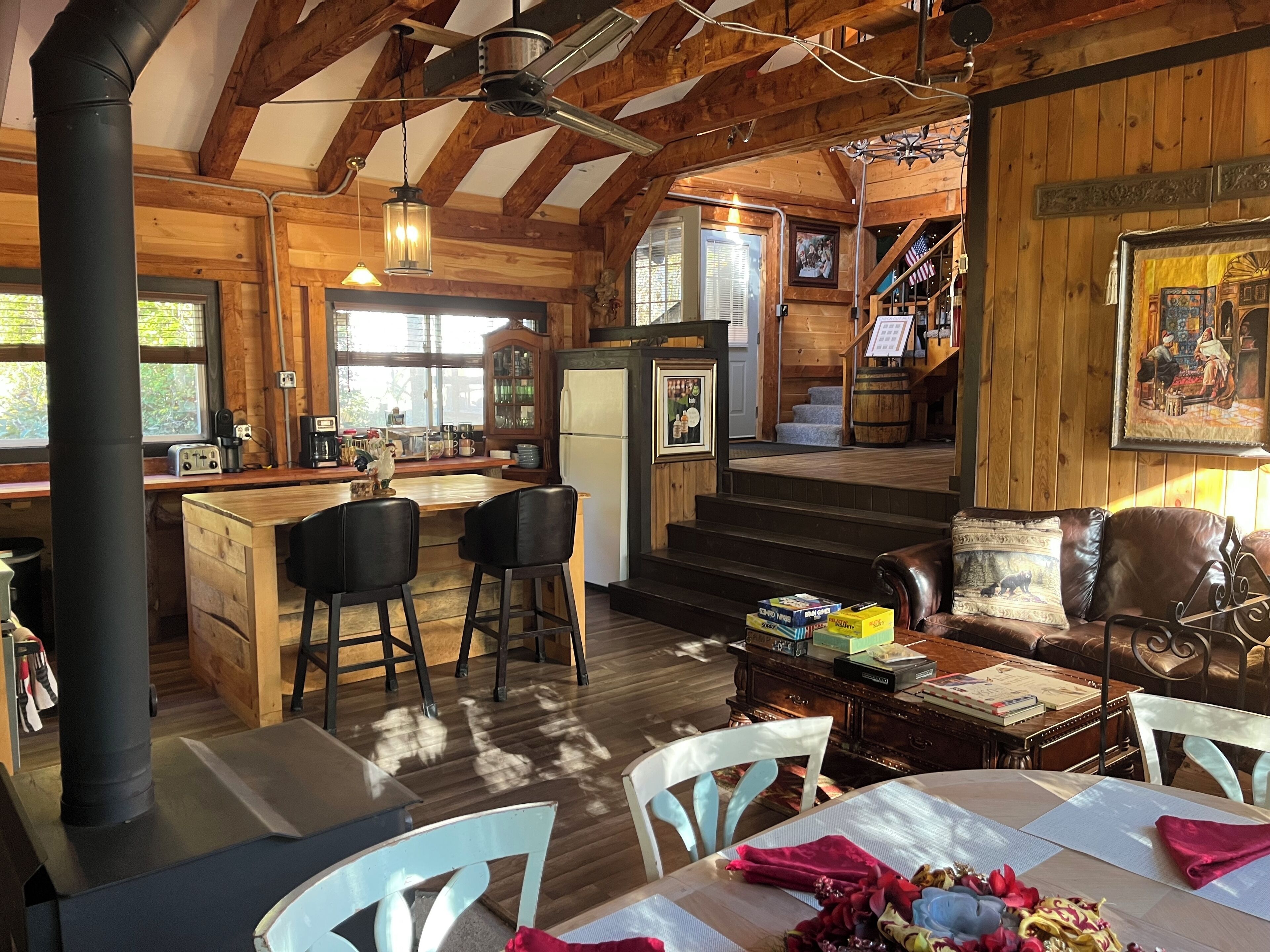 A rustic cabin interior with a wooden dining area, kitchen, and a staircase leading to a loft.