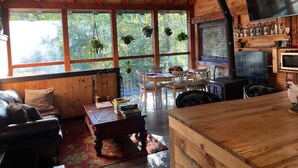 Een rustiek houten interieur met een houten plafond, grote ramen, een eethoek en een keuken met televisie en bar.
