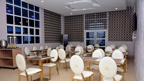 Un comedor con varias mesas y sillas, una barra de buffet con alimentos, y una pared con diseño.