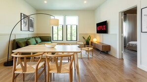 A modern living room with a dining area, a sofa, a TV, and a plant. - HOMA-Comfort&Style-1BR-Spacious-Natural Light-FeelHome-A/C-SelfCheckIn-Metro (Montréal)