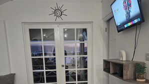 Ein Wohnzimmer mit einer Couch, einem Couchtisch, einem an der Wand befestigten Fernseher, einer Wanddekoration in Form einer Sonne und einer Glastür, die einen Blick ins Freie ermöglicht.