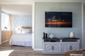 A bedroom with a bed, a nightstand, a desk with a lamp, and a large painting on the wall.