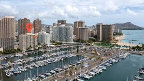 A marina with numerous boats docked, surrounded by high-rise buildings and a beach in the background.