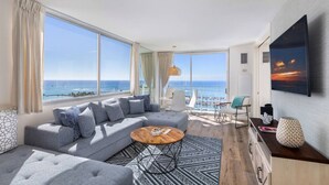 A modern living room with a large gray sectional sofa, a round coffee table, and a view of the ocean.