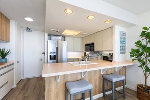 A modern kitchen with a central island, stainless steel appliances, and a welcoming sign. - Ilikai Collection # 12. Corner Oceanfront condo ! (Honolulu)