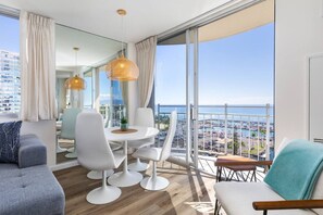 A modern hotel room with a balcony, a dining area, and a view of the city and sea. - Ilikai Collection # 12. Corner Oceanfront condo ! (Honolulu)