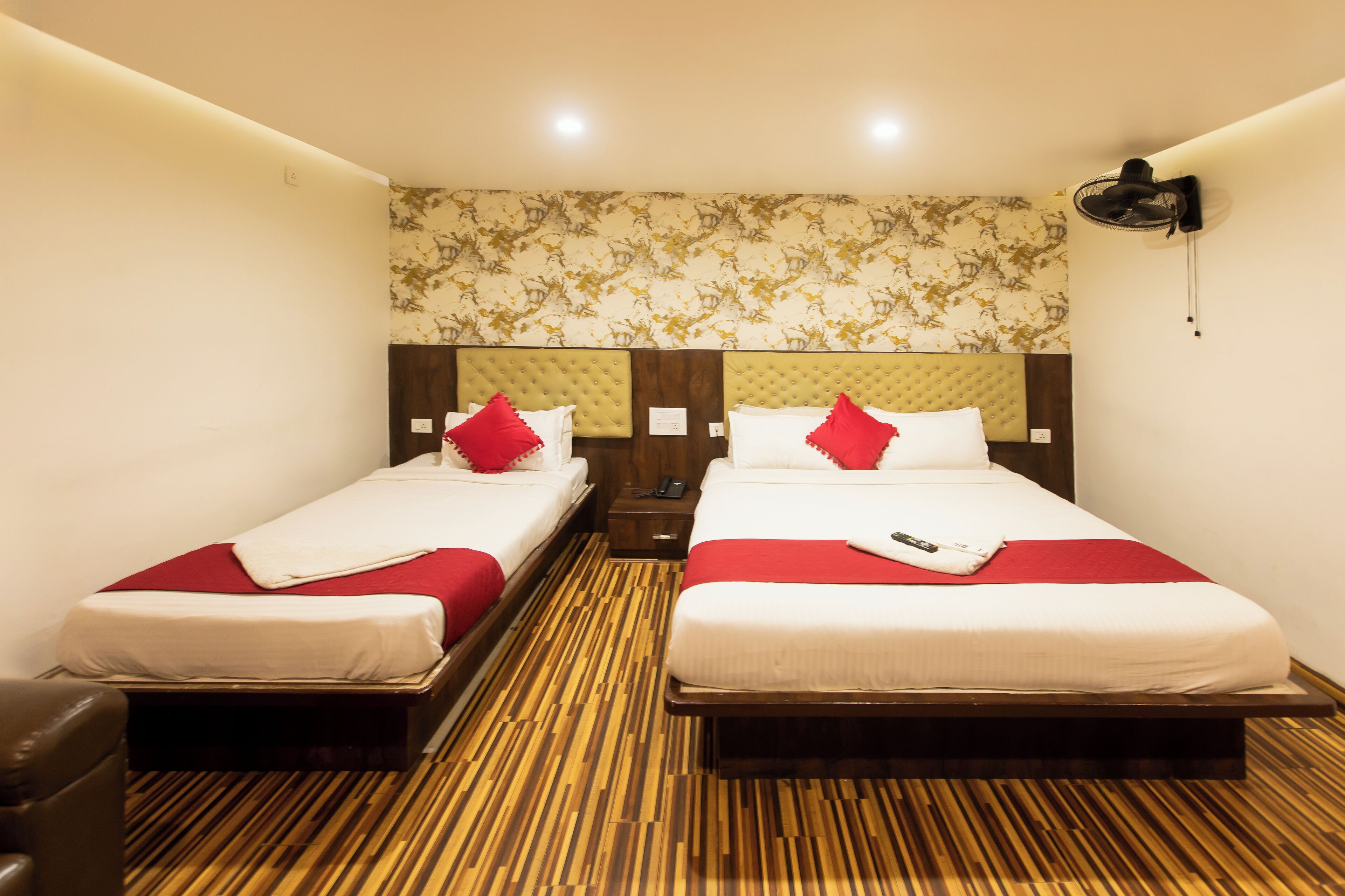 Une chambre d’hôtel avec deux lits, chacun agrémenté d’un oreiller rouge et de draps blancs. La chambre est dotée d’un plancher en bois et d’un papier peint à motifs sur le mur.