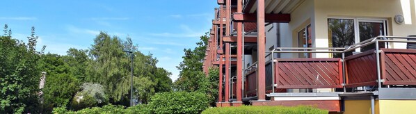 A modern building with a balcony, surrounded by lush greenery.