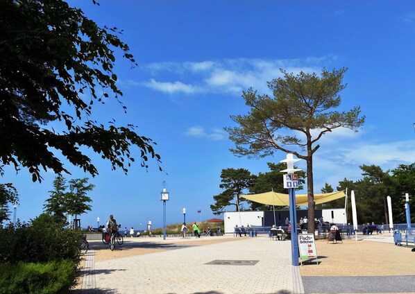 A coastal promenade with a weather station, seating areas, and a sign indicating a restaurant.