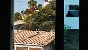 A coastal view from a window overlooking a beach, palm trees, and buildings. - Locals Taghazout Surfcamp (Taghazout)