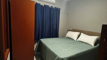 Quarto com cama, ventoinha no teto, ar condicionado e guarda-roupa de madeira.