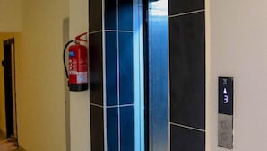 An elevator with a digital display showing the number 3, a fire extinguisher mounted on the wall, and a door with a blue and black panel design.