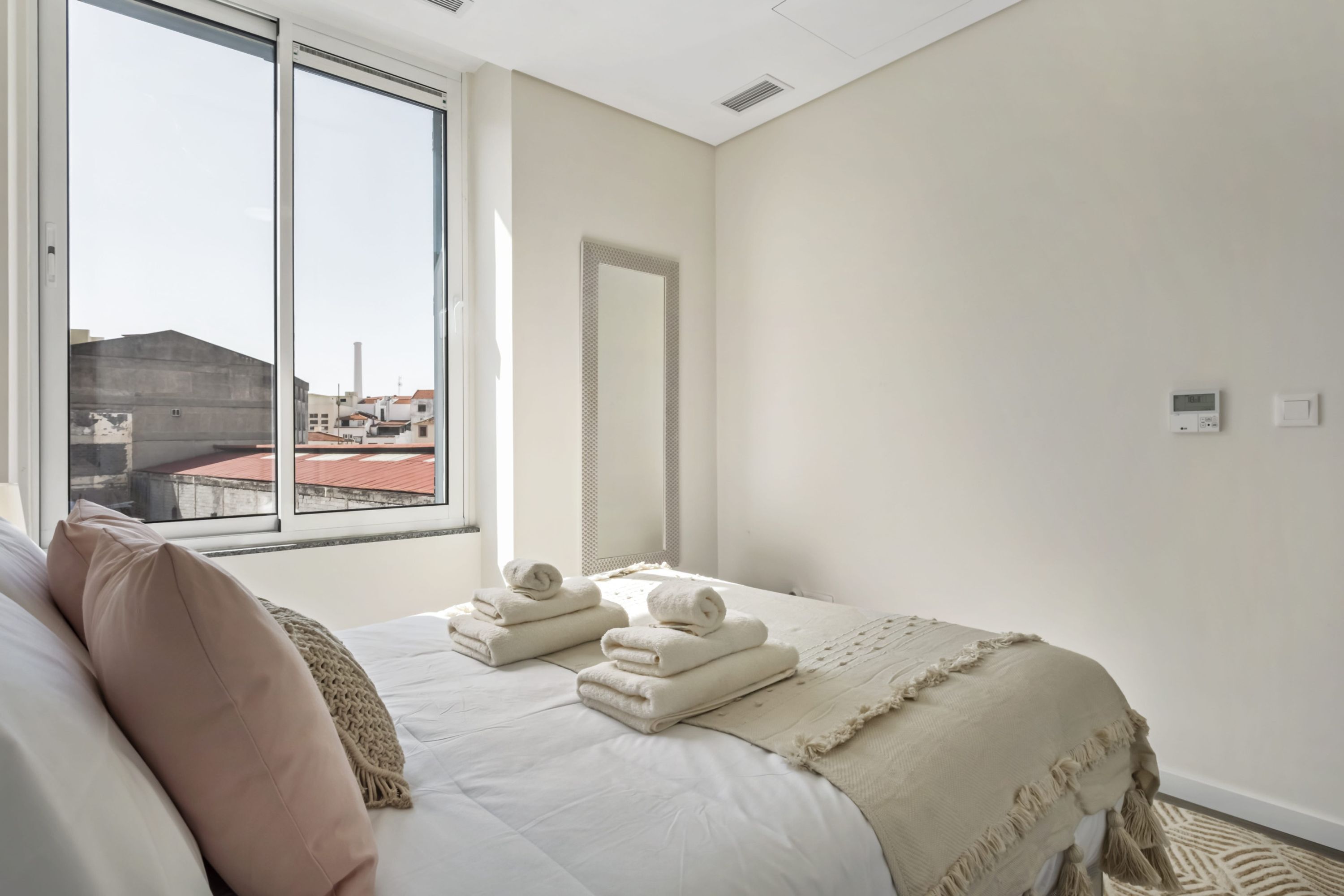 A bedroom with a large window, a bed with neatly folded towels, and a view of buildings outside.