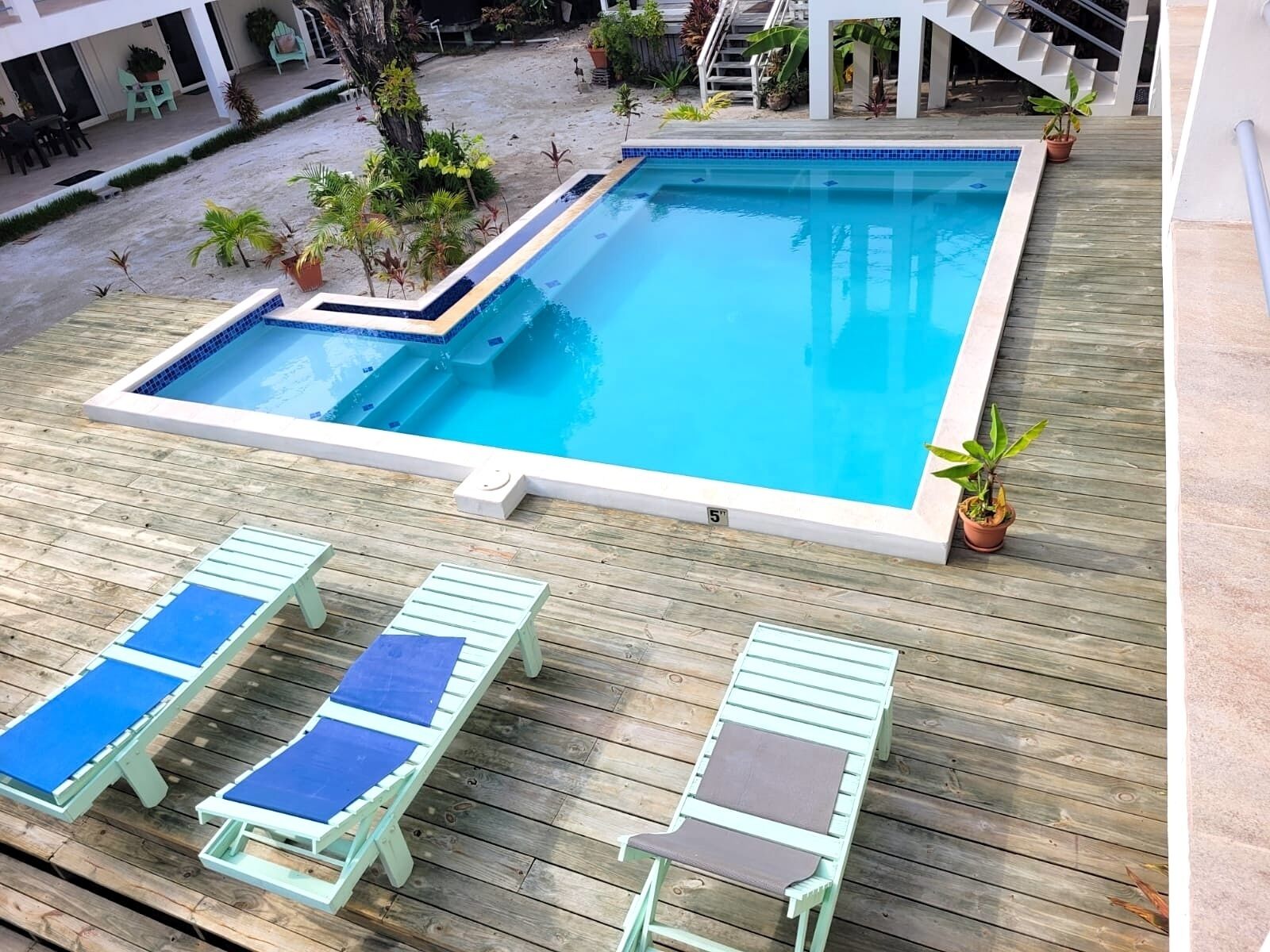 A rectangular pool with a tiled edge, surrounded by a wooden deck. There are lounge chairs with blue and brown cushions.