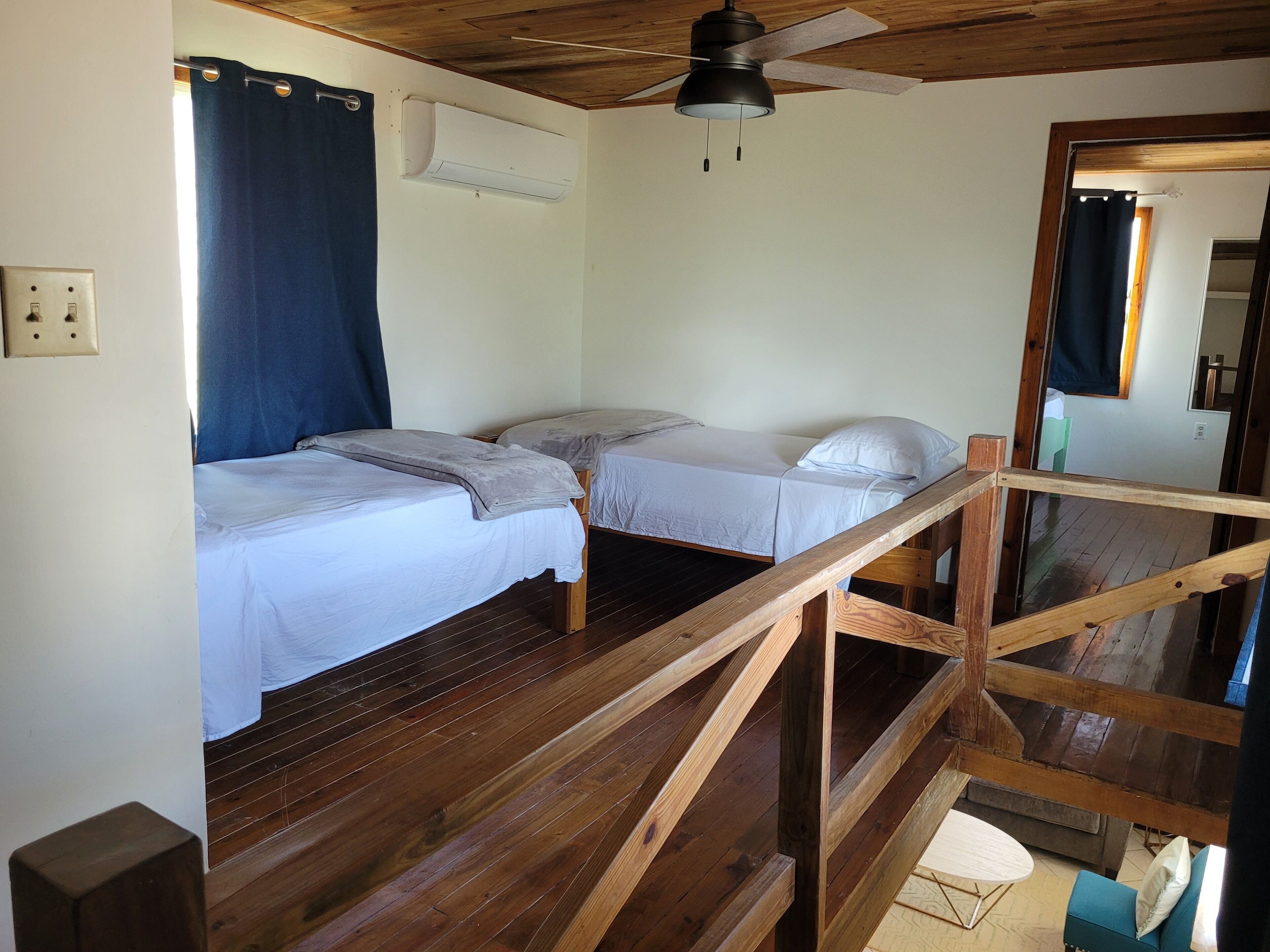 A room with two wooden bunk beds, a ceiling fan, an air conditioning unit, and a wooden staircase.