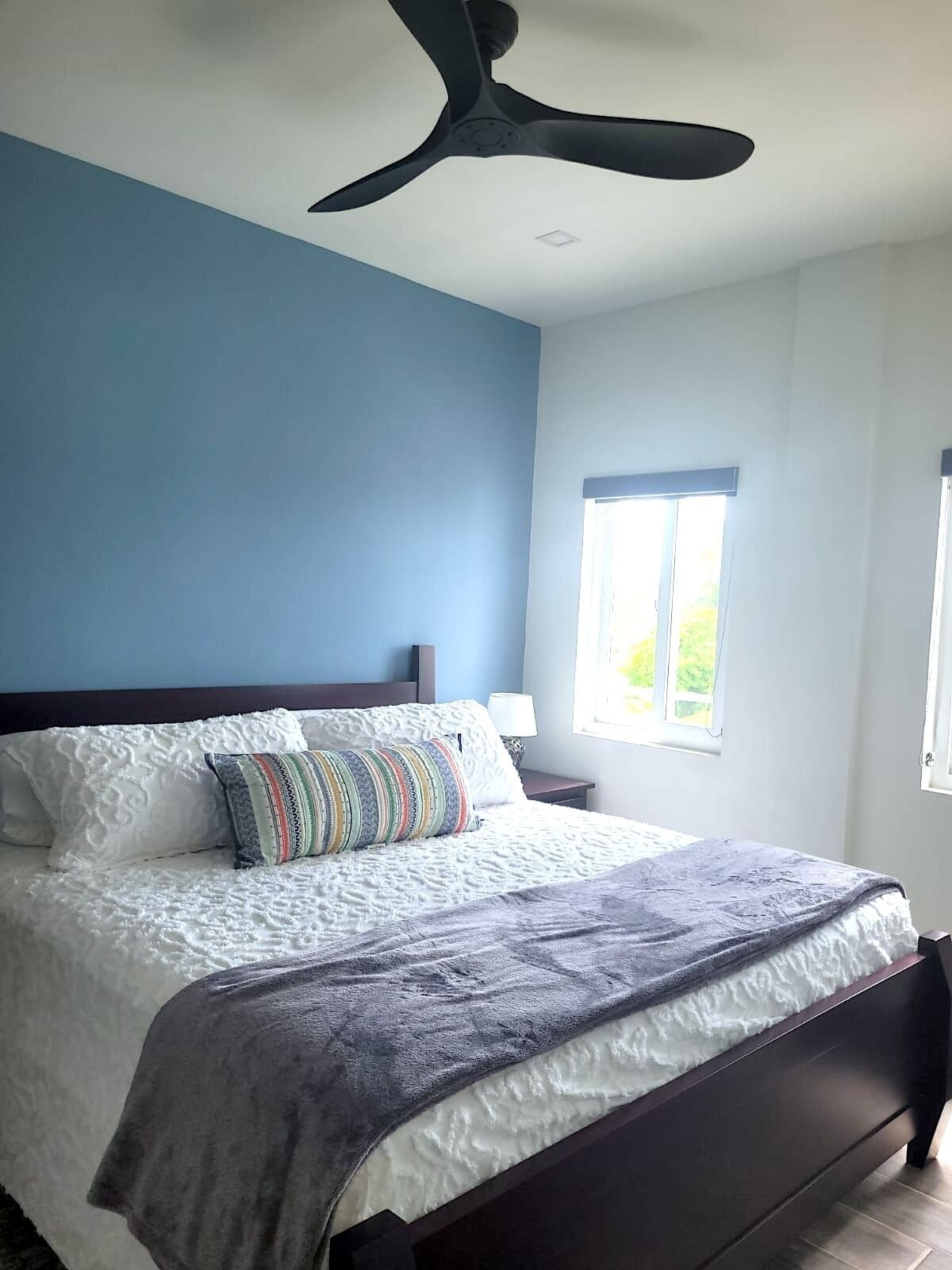 A bedroom with a bed, a ceiling fan, a window, and a nightstand.