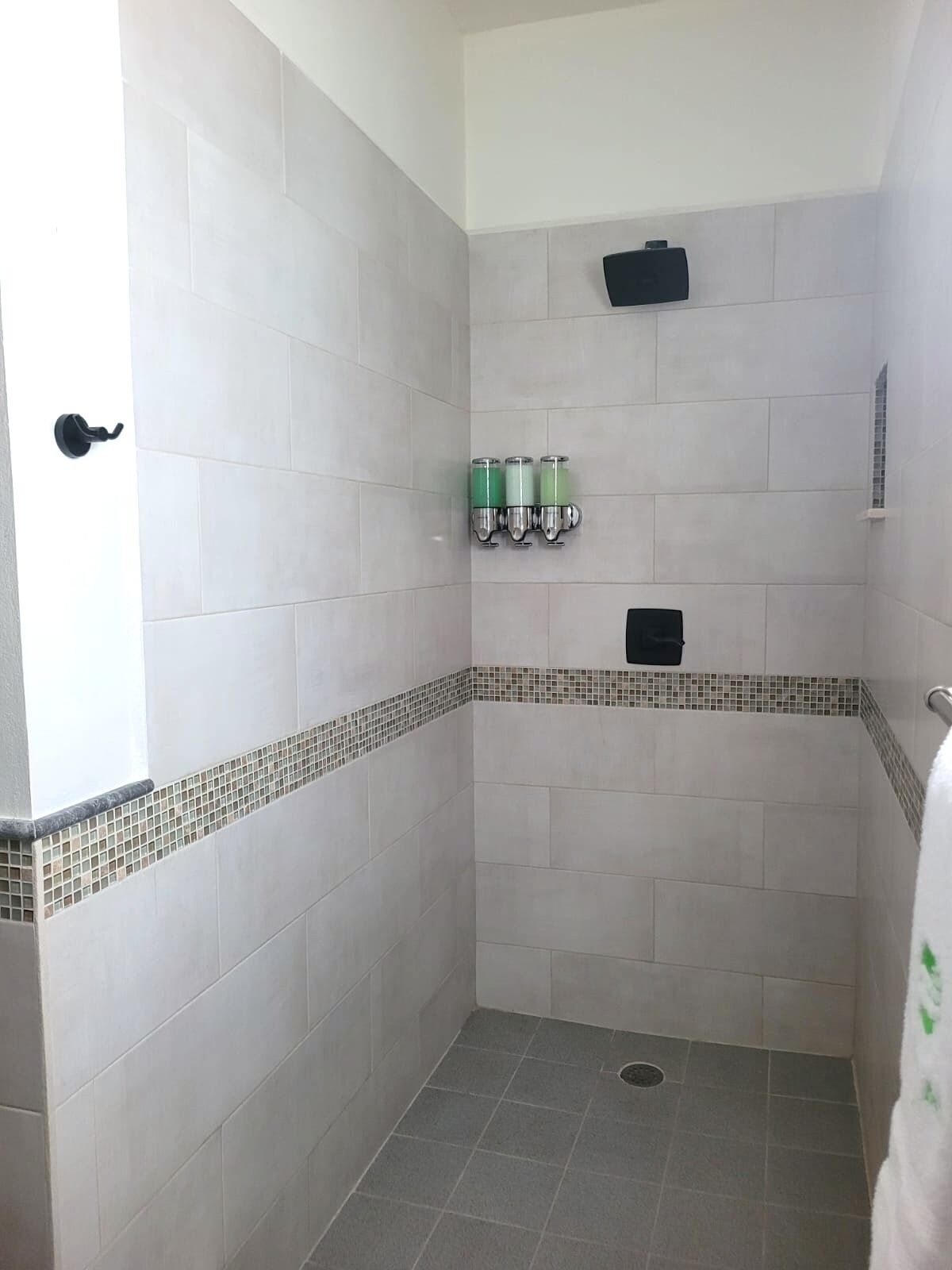 A small, enclosed shower area with white tiles, a drain, and a black towel rack.